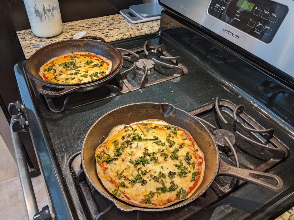 two cast iron skillets with sourdough pizza crust topped with garden veggies.
