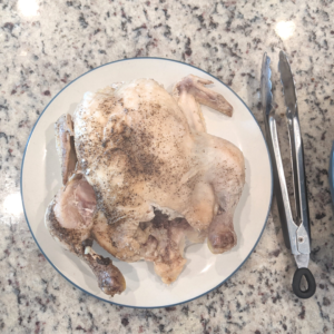 Whole chicken on a plate next to a pair of tongs on a kitchen counter