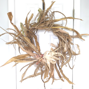 fall wreath mad with corn stalks and husks from glass gem corn hanging on a white door.