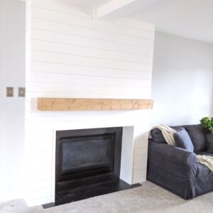 white shiplap fireplace with faux beam mantel with a blue couch next to it
