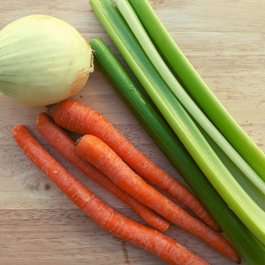 celery stalks, long carrots, and one whole onion on a wooden cutting board