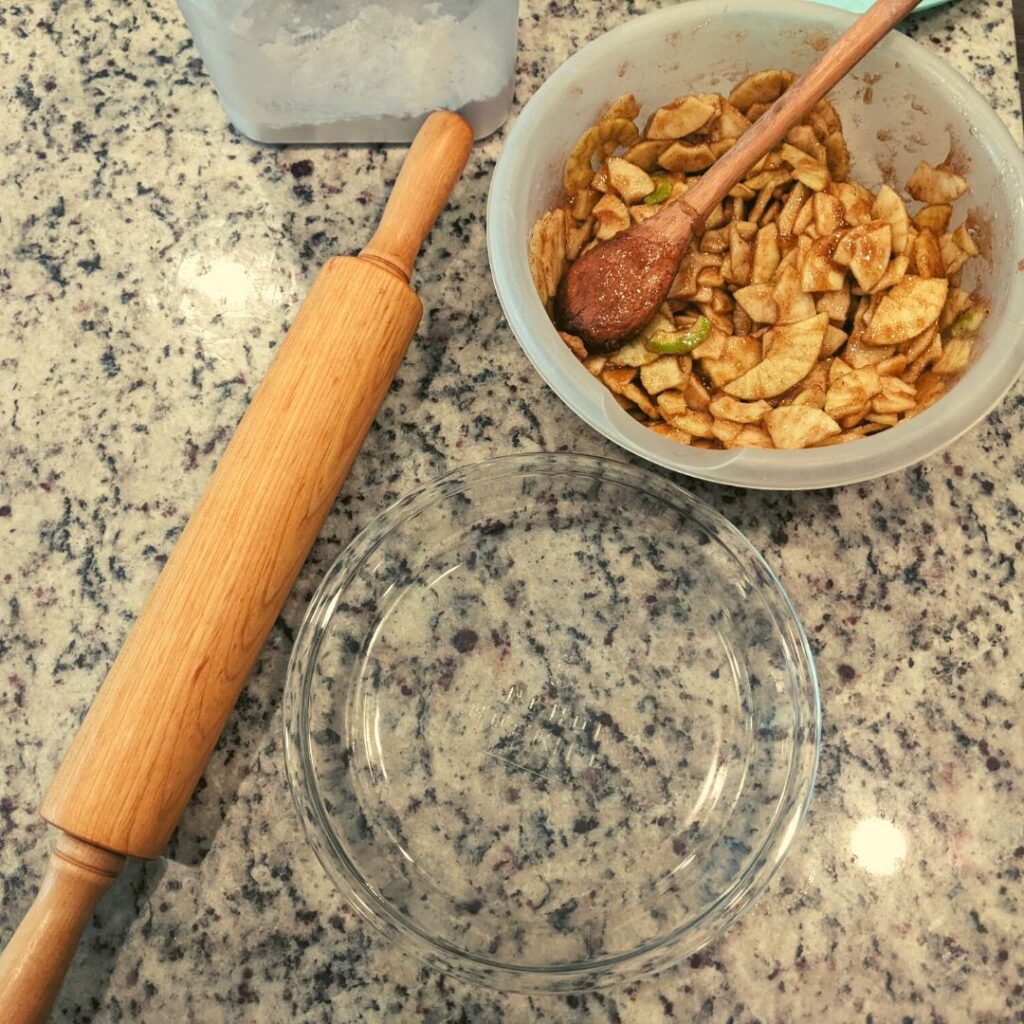 rolling pin next to a cinnamon apple slices and a pie pan