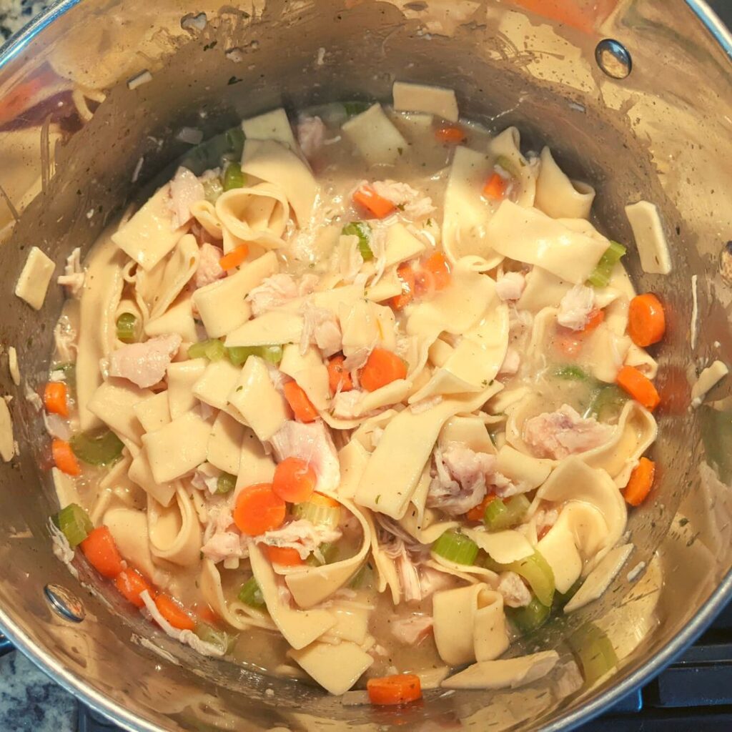 chicken noodle soup with leftover chicken, carrots, celery and onions inside a large stock pot. 