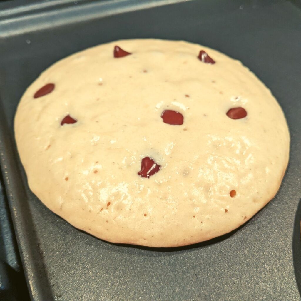 large fluffy whole wheat pancake with chocolate chips and bubbles in it. ready to flip