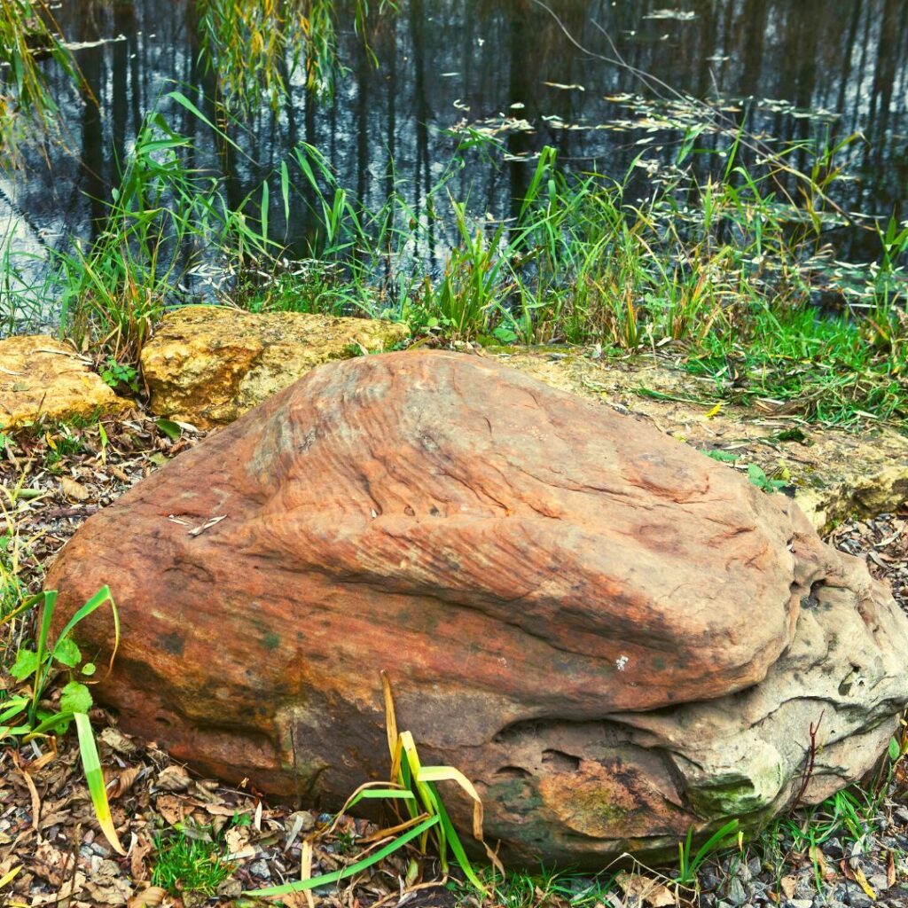 large rock sitting next to a pond