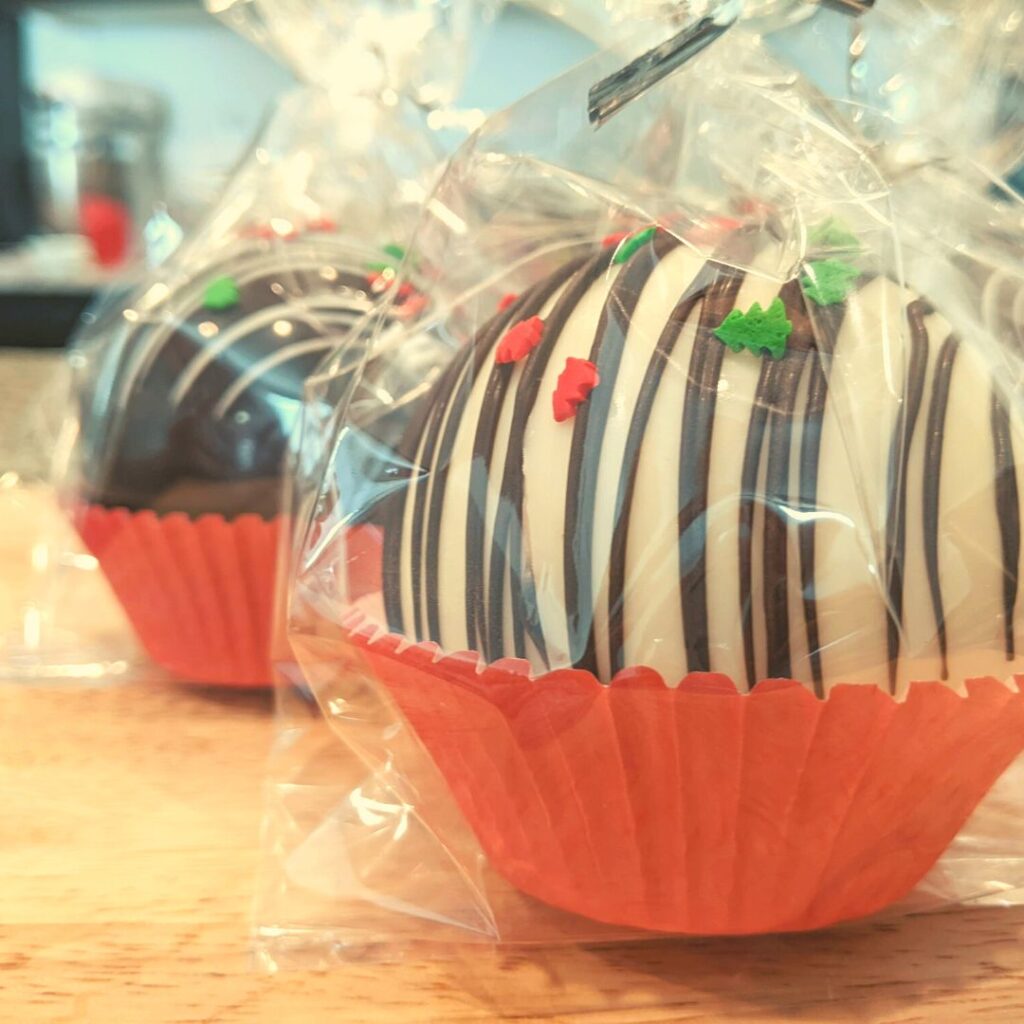 hot chocolate bombs in red cup cake liners wrapped in cellophane bags on a wooden cutting board