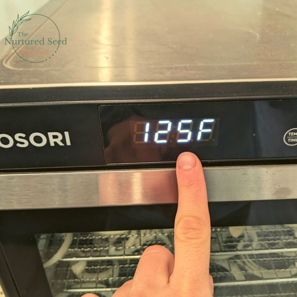 woman's hand pointing at the temperature on a cosori dehydrator that says 125 degrees f