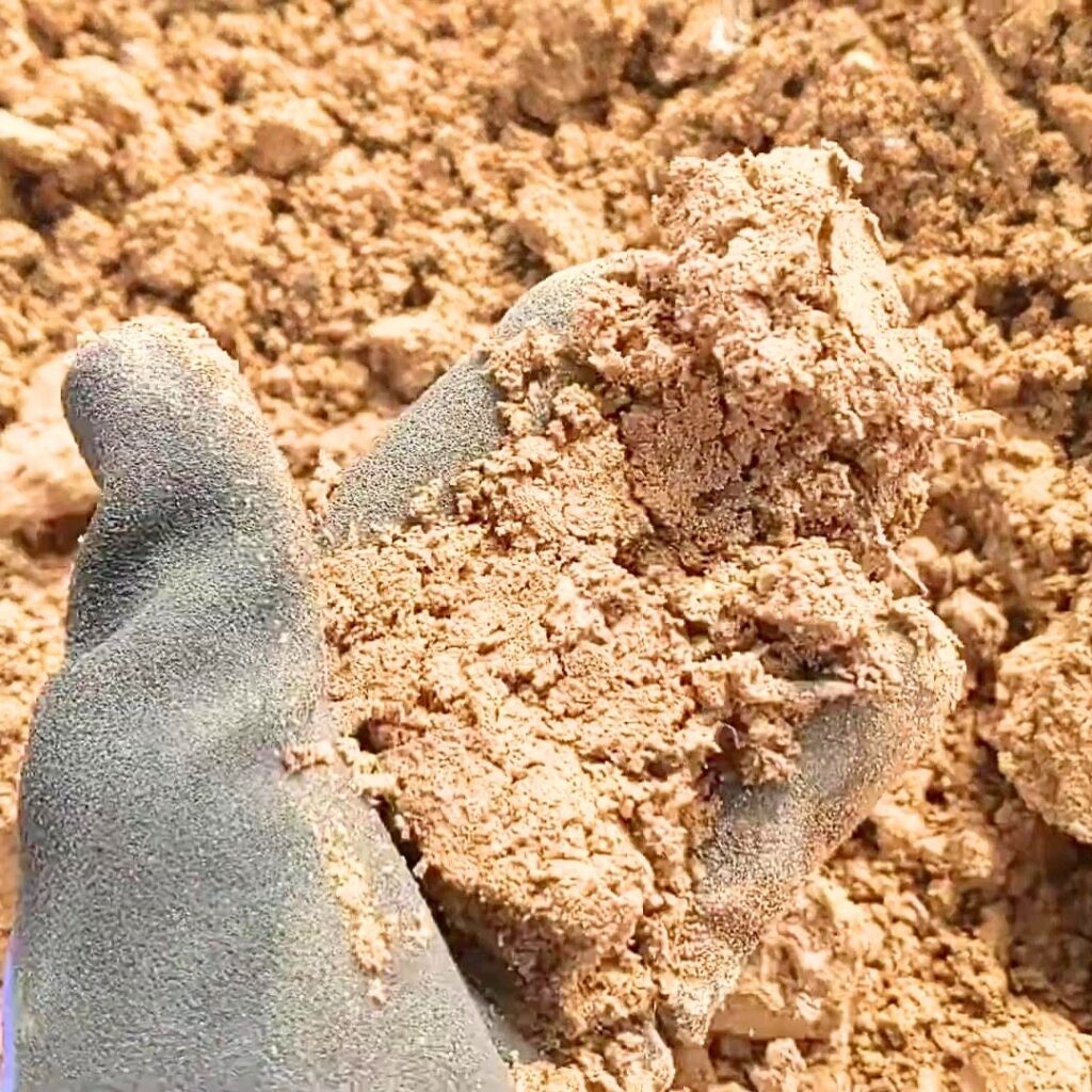 gloved hand holding a sandy soil sample