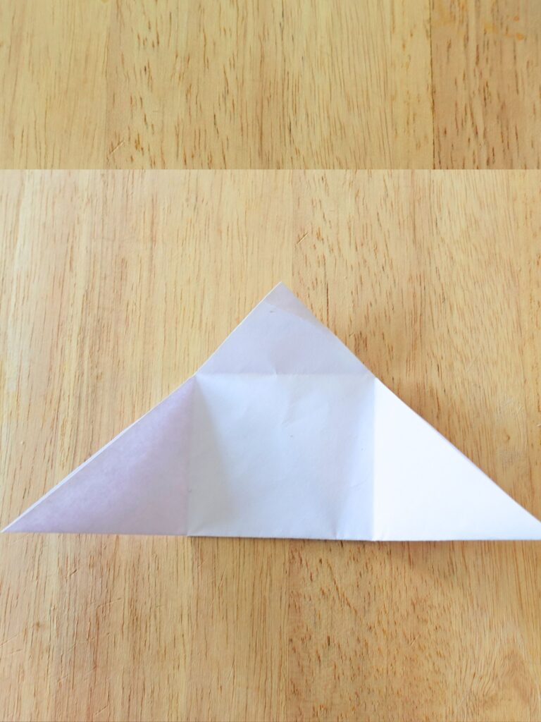 square piece of paper folded in half to look like a triangle on top of a wooden cutting board