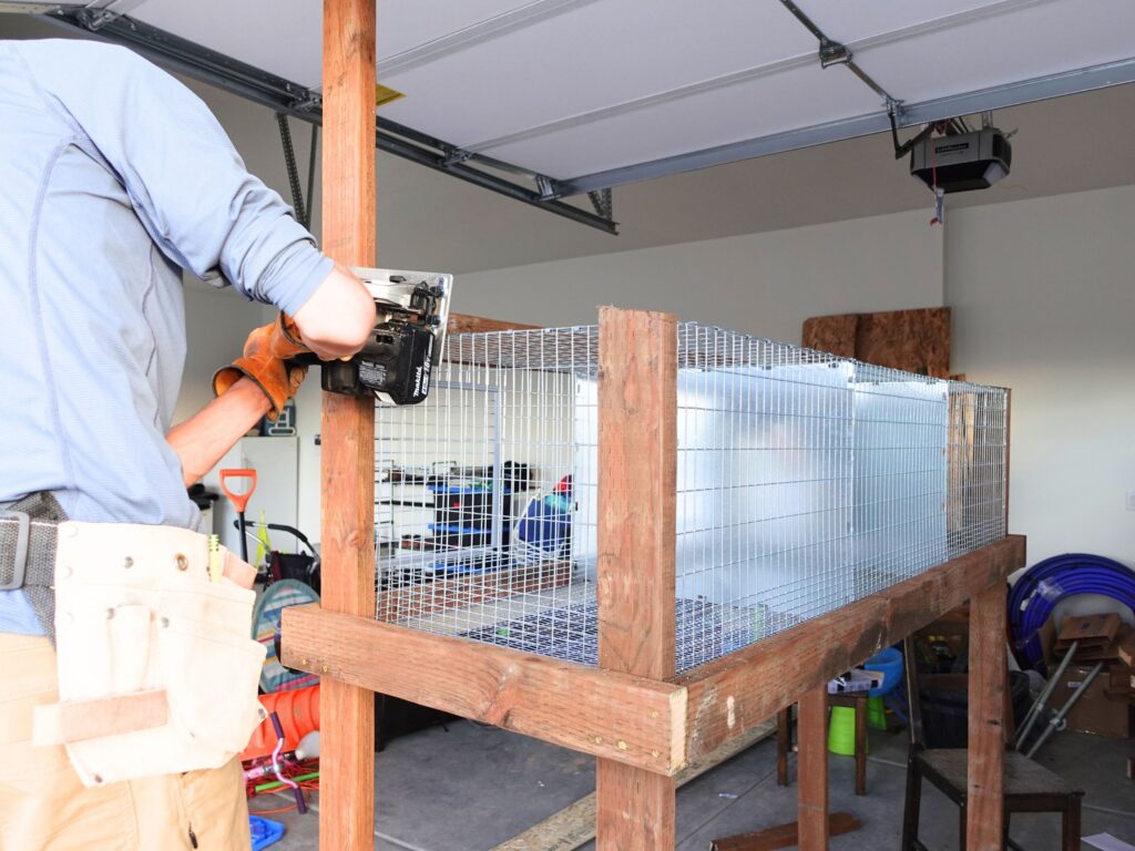 man using saw to cut the front legs on the rabbit hutch with kw cages inside